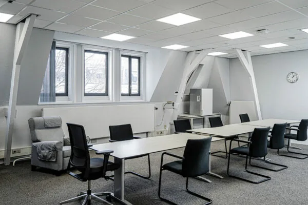 Vergaderruimte aan de Burgemeester van Karnebeeklaan met moderne inrichting, witte tafels en zwarte stoelen.